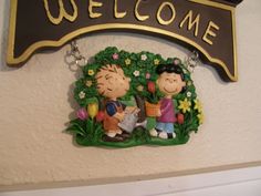 a welcome sign hanging from the side of a wall with two children holding watering cans