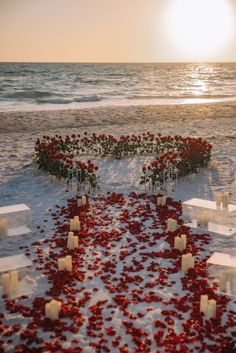 the sun is setting on an empty beach with red flowers and candles in the sand