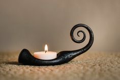 a candle that is sitting on the ground next to a black hook with a white candle in it