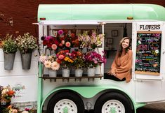 a woman sitting in the back of a food truck with flowers on display behind it