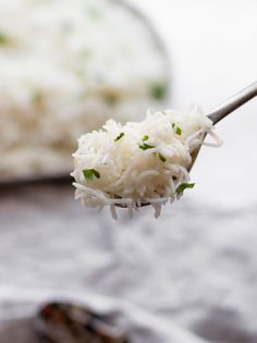 a spoon full of white rice on top of a plate with another dish in the background