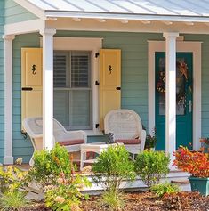 a blue house with yellow shutters and two chairs on the front porch next to it