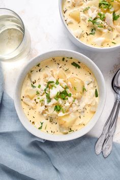 two bowls filled with soup on top of a white table next to silver spoons