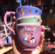 someone is holding up three cups with cartoon characters on them in front of other items