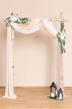 an arch decorated with white flowers and greenery for a wedding ceremony in the middle of a room