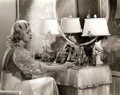 a woman sitting at a table with lots of bottles on it and a mirror in the background