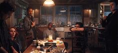 a group of people sitting around a table in a kitchen at night with lights on