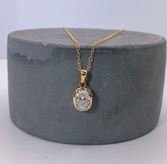 a gold necklace with a white diamond in the center on a grey stone surface,