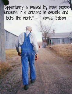 a man walking down a dirt road next to a tall gray building with a poem written on it