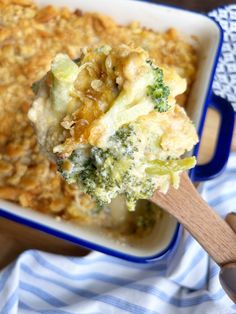 a casserole dish with broccoli and cheese in it is being held by a wooden spoon