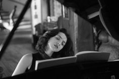 a woman sitting at a piano with her eyes closed and reading a book in front of her