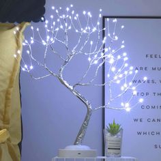 a white tree with lights on it sitting next to a poster and potted plant