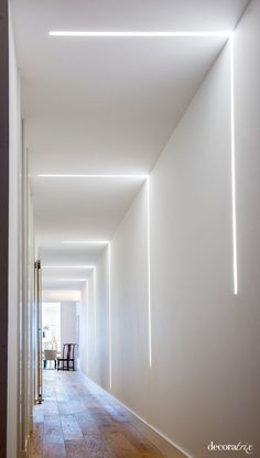 an empty hallway with white walls and wooden floors is lit by bright lights from the ceiling