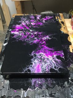 two large black and purple paintings sitting on top of a wooden table covered in paint