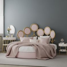 a bed with pink sheets and pillows in a gray room next to two round mirrors