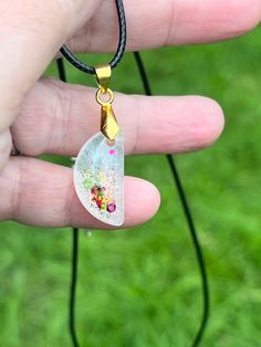 a hand holding a glass pendant with flowers on it's side and green grass in the background