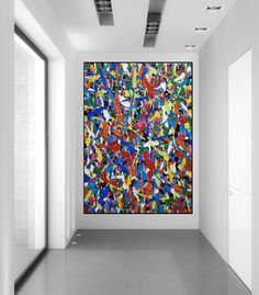 an abstract painting hangs in the middle of a room with white walls and flooring