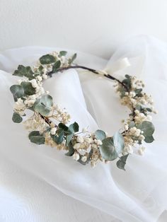 a white flower and leaf headband on top of a white cloth covered bed sheet