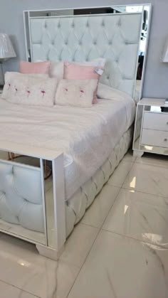 a white bed with pink pillows and two nightstands in front of the headboard