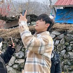 two people standing next to each other taking pictures with their cell phones in front of a stone wall