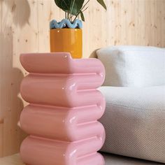 a pink vase sitting on top of a table next to a white chair and potted plant