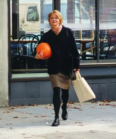 a woman walking down the street carrying shopping bags and a basketball in her hand while holding an orange ball