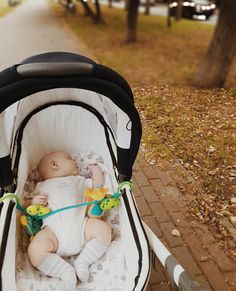 a baby laying in a stroller on the side of a road next to trees