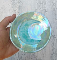 a hand holding a glass bowl on top of a white wooden table next to a wall