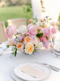 the table is set with white plates and silverware, pink and orange flowers in vases