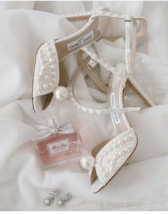 a pair of shoes and a bottle of perfume on a white bed sheet with pearls