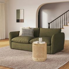 a green couch sitting on top of a wooden floor next to a stair case in a living room