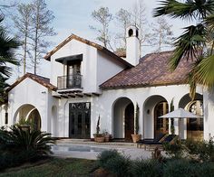 a large white house with lots of windows and plants in the front yard, surrounded by palm trees