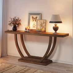 a wooden table with candles and pictures on it in front of a white wall next to a lamp