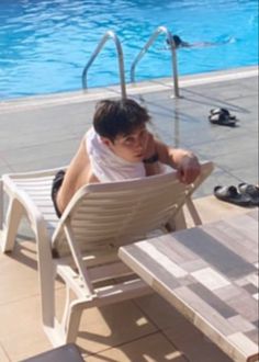 a man sitting in a chair next to a swimming pool with his feet on the table