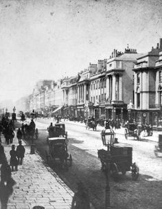 an old black and white photo of people walking down the street with horse drawn carriages