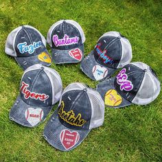 six baseball caps with the words together on them in different colors and sizes, sitting on green grass