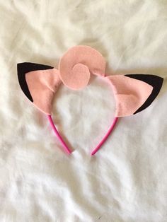 a pink and black cat ears headband laying on top of a white bed sheet