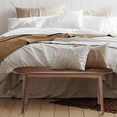 a bed with white linens and pillows on top of it, along with a wooden bench