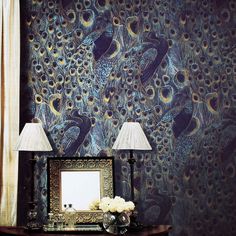 two lamps and a mirror on a table in front of a wall with a peacock pattern