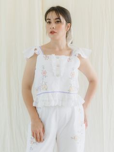 Our one-of-a-kind Hand Embroidered Floral Crop Top and Pants Set is a beautiful addition to any wardrobe. The crop top features colorful floral embroidery, an even hemline with lace, sleeveless straps with frills, and a stunning design that will catch everyone's attention. Made from vintage textiles, the pant has an elastic waistband at the sides, one button behind the waistband, and a high waist pattern with subtle floral embroidery.  The white cotton fabric is both comfortable and breathable. Feminine Cotton Embroidered Top For Daywear, Fitted Embroidered Top With Floral Design For Daywear, Spring Matching Set Tops, White Matching Set Top For Spring, Summer Cotton Sets With Floral Embroidery, Spring Daywear Tops Matching Set, Feminine Floral Embroidery Bottoms For Summer, White Floral Embroidery Top For Garden Party, Fitted Floral Embroidered Top For Daywear