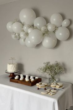 a table topped with cupcakes and white balloons