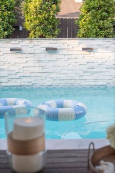 a candle sitting on top of a wooden table next to a pool with inflatable rafts