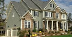 a large gray house with lots of windows and landscaping around the front door is shown