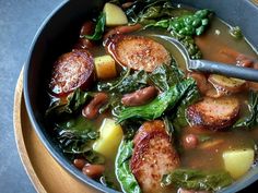 a bowl filled with meat and vegetables on top of a wooden table next to a spoon