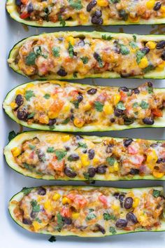 stuffed zucchini boats filled with black beans, cheese and other toppings in a white baking dish