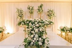 a table with white flowers and greenery on it in front of a gold chair