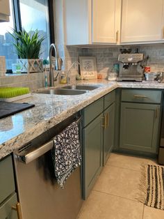 a kitchen with green cabinets and marble counter tops, an island sink and dishwasher