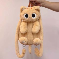 a person holding a stuffed animal in the shape of a cat with eyes on it's back