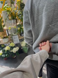 two people are holding hands in front of some potted plants at a flower shop