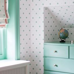 a green dresser with a globe on top of it next to a wallpapered room